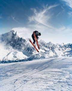 A person on red skis in mid-air. They are angled downward with their feet kicked up so you can see the bottom of their skis.