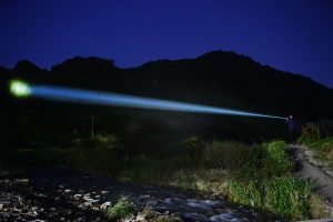 An image from the Nitecore P35i series of someone using their LEP flashlight to look at a far away cluster of trees.