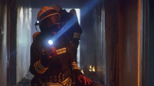 Firefighters in protective gear illuminating burnt corridor with flashlights and inspecting walls during rescue operation with their flashlight