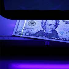 A UV strip glows on a $20 bill under a UV light