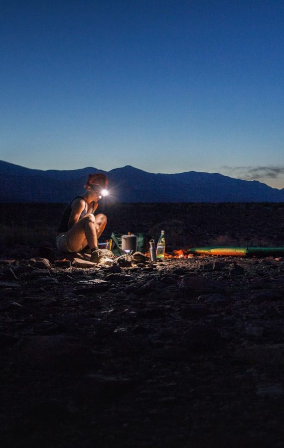 A woman sits by her tent with a headlamp on.
