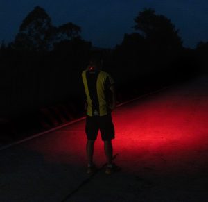 A person stands in the middle of the path with their headlamp on red mode.
